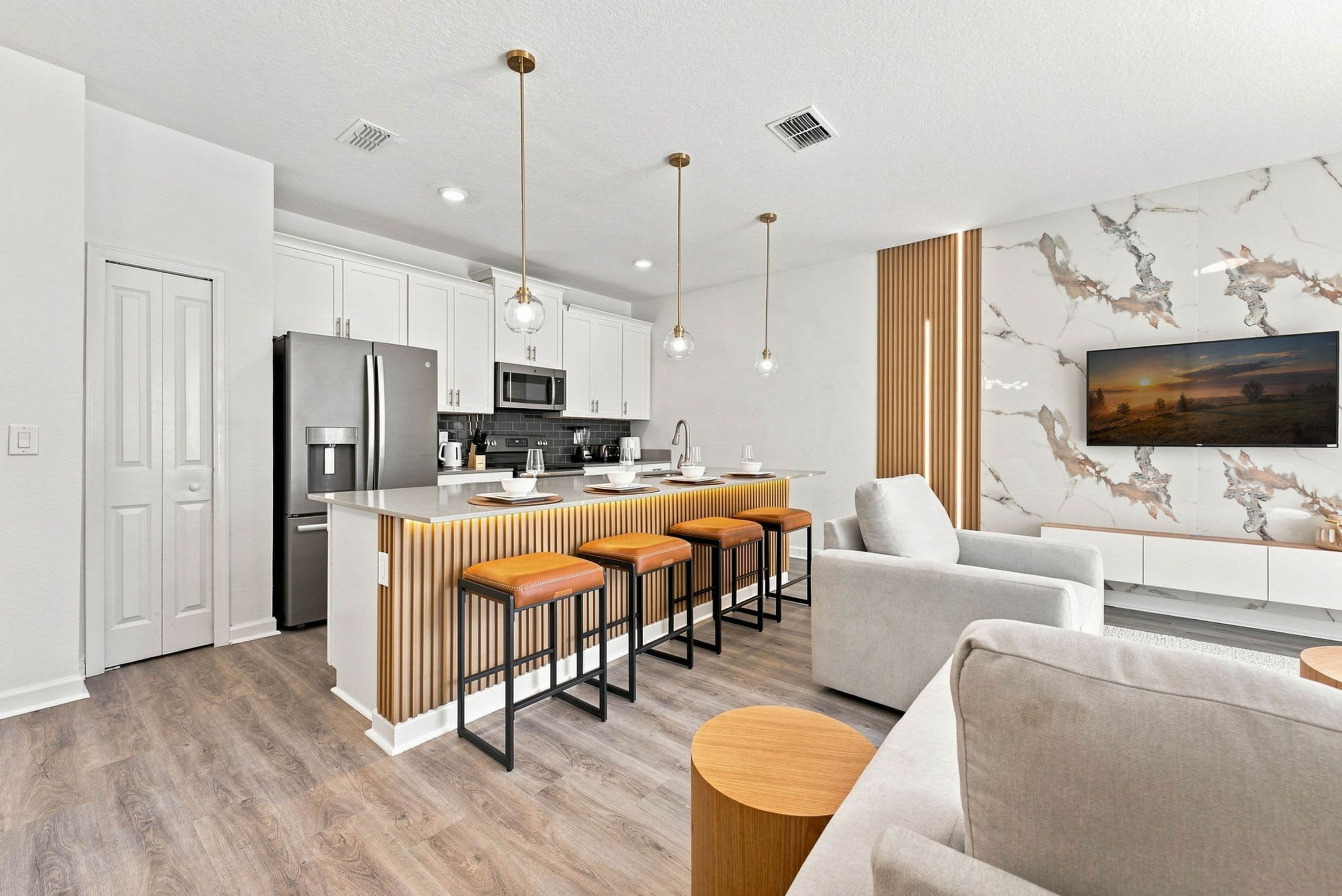 A modern kitchen with a central island, bar stools, and a dining area with a sofa and a round wooden side table.