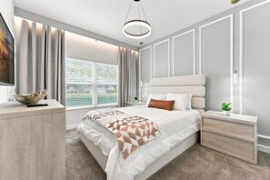 Un dormitorio moderno con una cama grande, mesitas de noche, una lámpara colgante y vistas a la vegetación por la ventana.