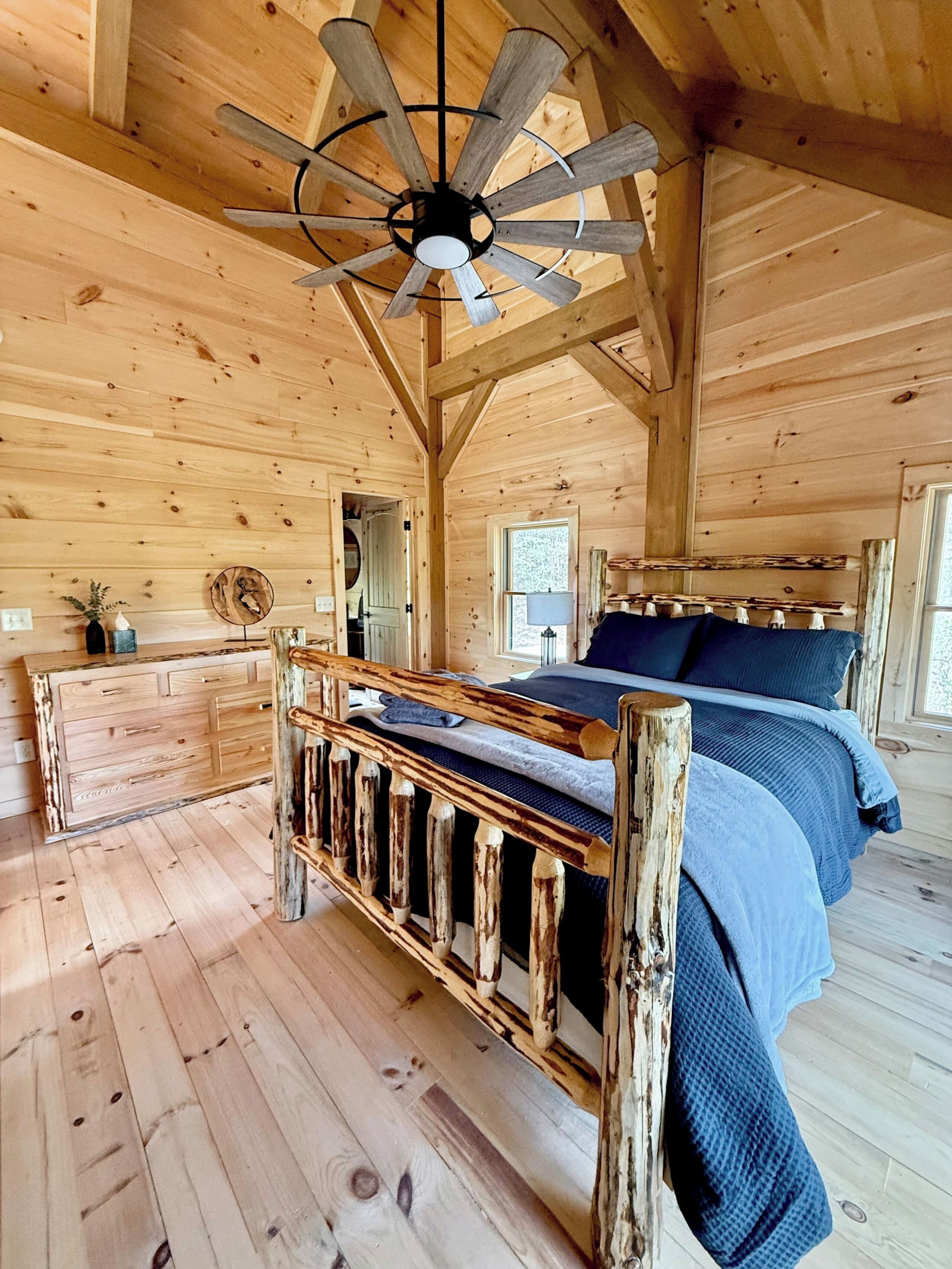 L’intérieur d’une cabane en bois, avec un lit, une commode, un ventilateur de plafond et une fenêtre.