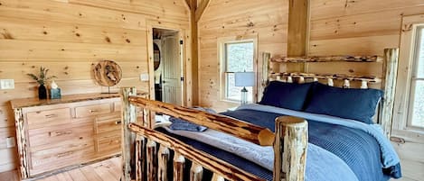 A wooden cabin interior with a bed, a dresser, a ceiling fan, and a window.