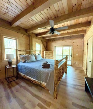 Un dormitorio de madera con cama, ventilador de techo y ventanas grandes.