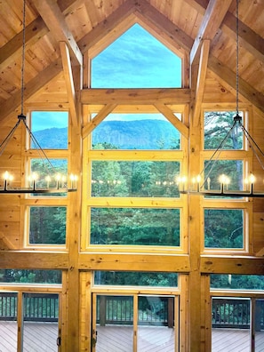 A wooden cabin with multiple windows offering views of a forested landscape. - Fantastic 4-bedroom, Spacious Timberframe Cabin in charming Lake Lure (Lake Lure)