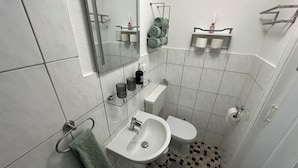Une petite salle de bain avec un lavabo blanc, des toilettes et un miroir au-dessus du lavabo.