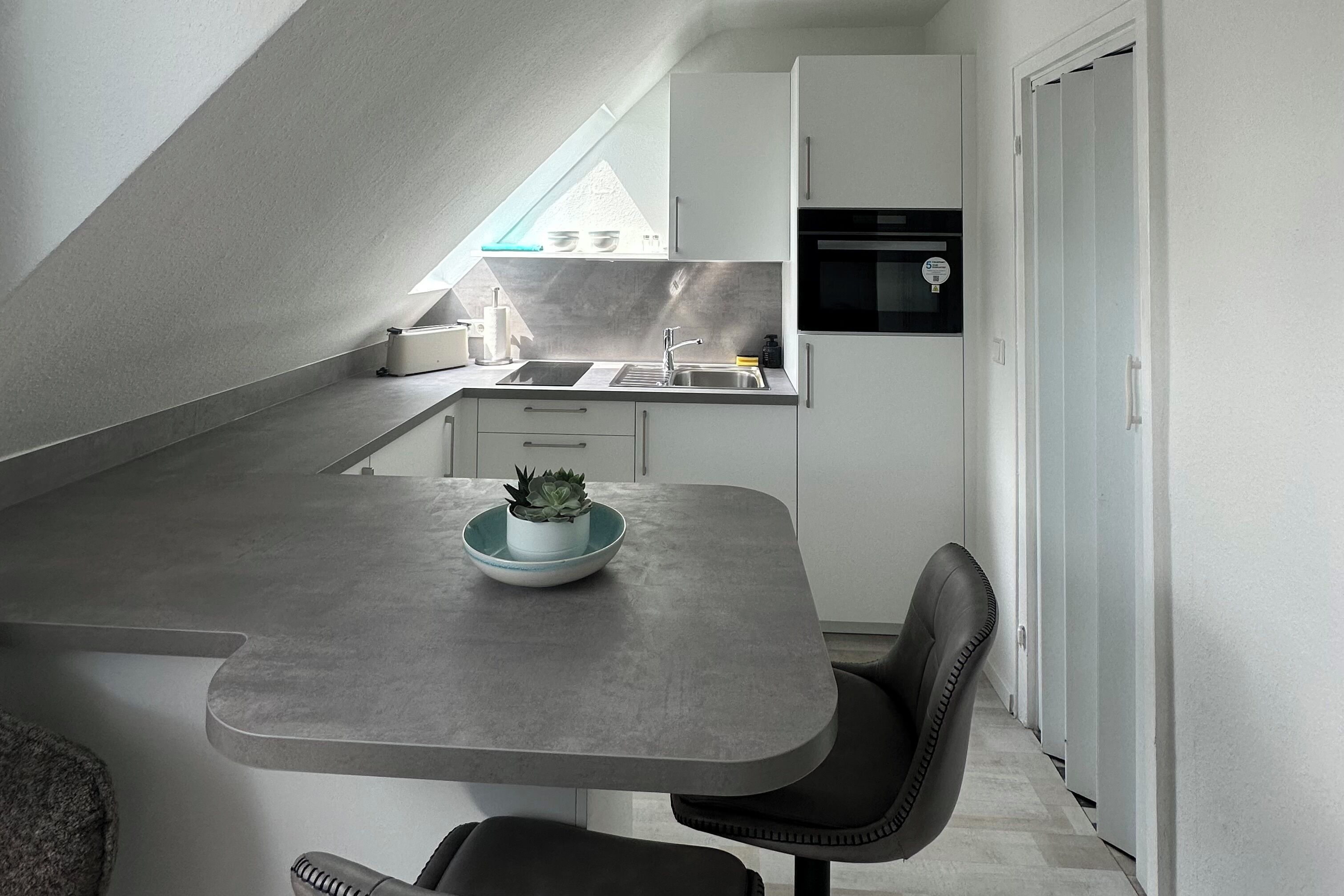 Eine kompakte Küche mit Backofen, Spüle und einer kleinen Essecke mit Tisch und Stuhl.