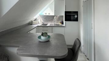Eine kompakte Küche mit Backofen, Spüle und einer kleinen Essecke mit Tisch und Stuhl.