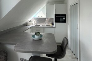 Une cuisine compacte équipée d’un four encastré, d’un évier et d’un petit coin repas avec une table et une chaise.