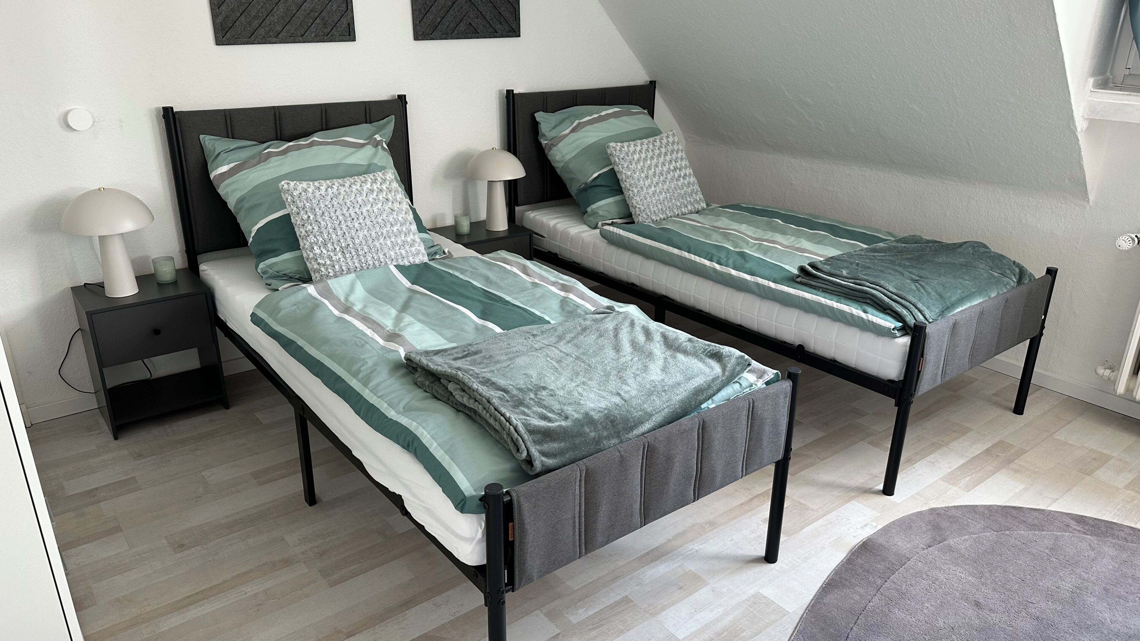 Ein Doppelzimmer mit zwei Einzelbetten, jeweils mit Kissen und einem Nachttisch mit Lampe.