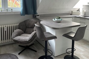 Una cocina moderna con una isla central, taburetes de bar y una silla.