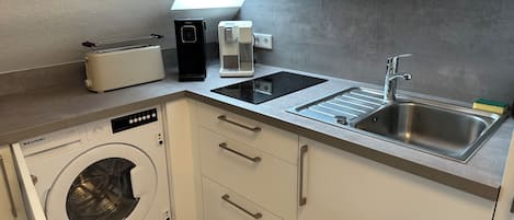 A compact kitchen with a washing machine, a coffee maker, and a sink.