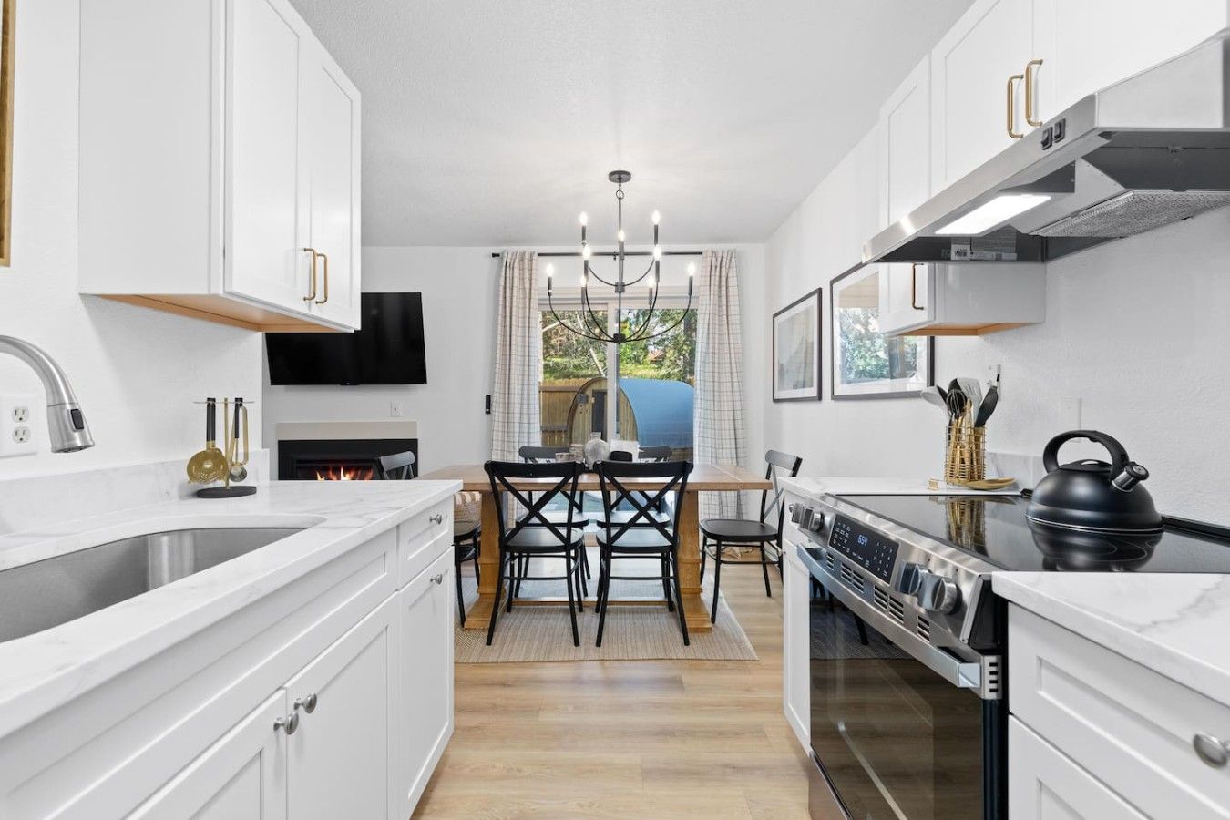 A modern kitchen with white cabinetry, a central island, a built-in oven, and a dining area with a table and chairs.