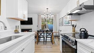 A modern kitchen with white cabinetry, a central island, a built-in oven, and a dining area with a table and chairs.