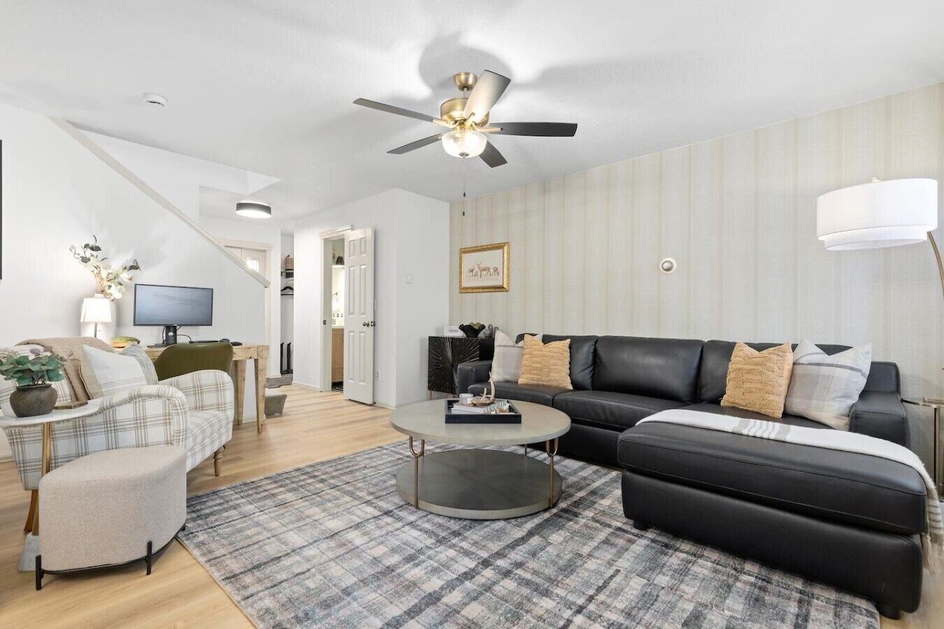 A modern living room with a sofa, armchair, coffee table, and a ceiling fan.