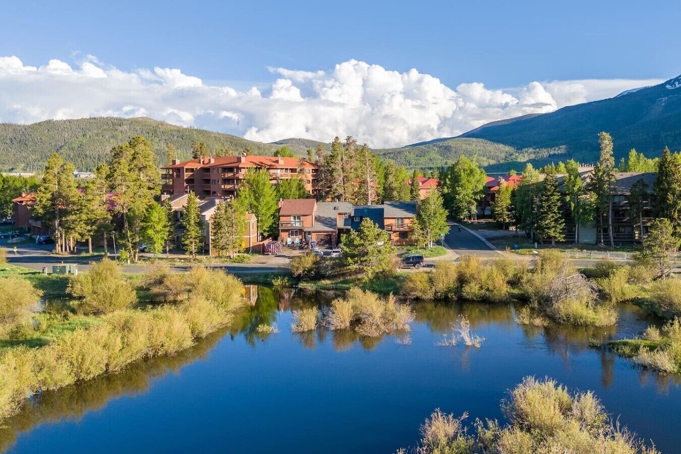 A lakeside hotel with multiple buildings, a clear sky, and surrounding mountains.