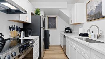 A modern kitchen with white cabinets, stainless steel appliances, and a marble countertop.