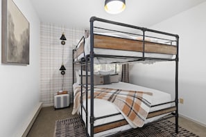 Un lit superposé avec une tête de lit, une lampe de chevet, une valise et un tapis à motifs.
