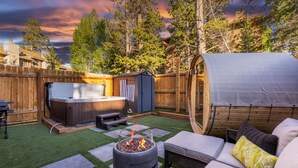 Ein Garten mit Whirlpool, überdachter Sitzgelegenheit und Feuerstelle.