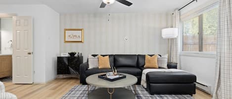 Un salon moderne avec un canapé en cuir noir, une table basse ronde et un ventilateur de plafond.
