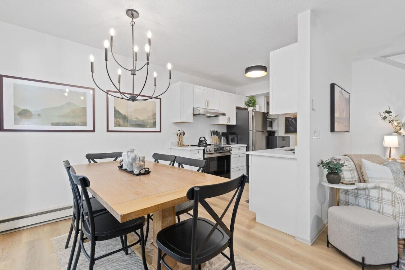 A modern kitchen with white cabinetry, a dining table with chairs, and a chandelier.