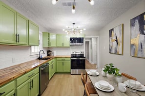 Una cocina moderna con armarios verdes, encimera de madera y una zona de comedor con mesa para cuatro.