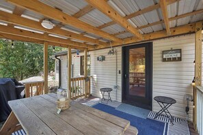 Ein überdachter Patio-Bereich mit einem Holztisch, einem Grill und einem Schild mit der Aufschrift 'Lake House'.