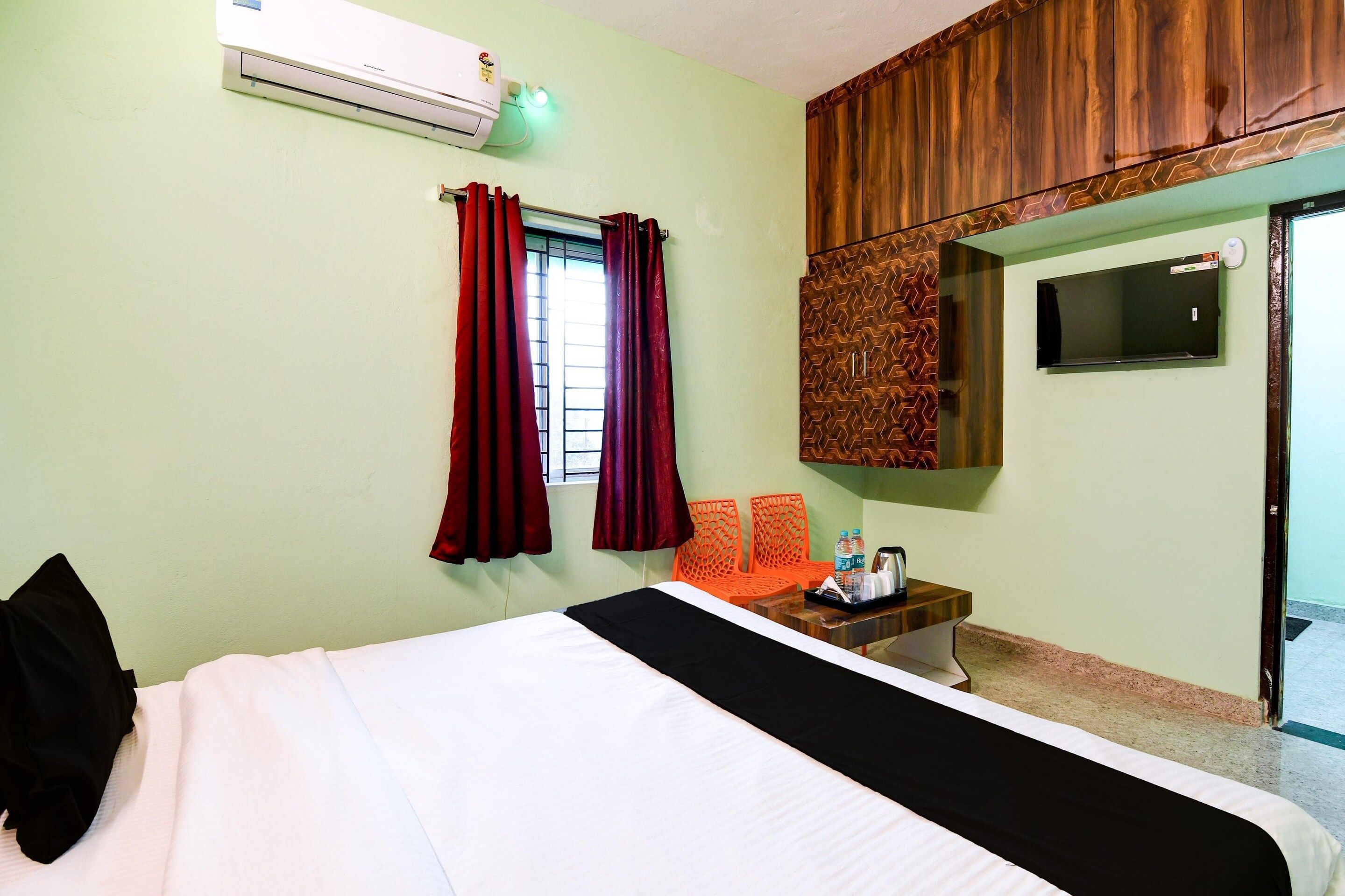 Ein Hotelzimmer mit einem Bett, einem Schreibtisch mit Wasserkocher, zwei orangefarbenen Sesseln, einem Fernseher an der Wand und einer Klimaanlage.