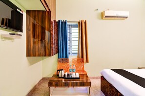 A hotel room with a bed, a wooden desk with a kettle and Bisleri water bottles, a TV, and an air conditioner. - Classic Star Light (Bhubaneshwar)
