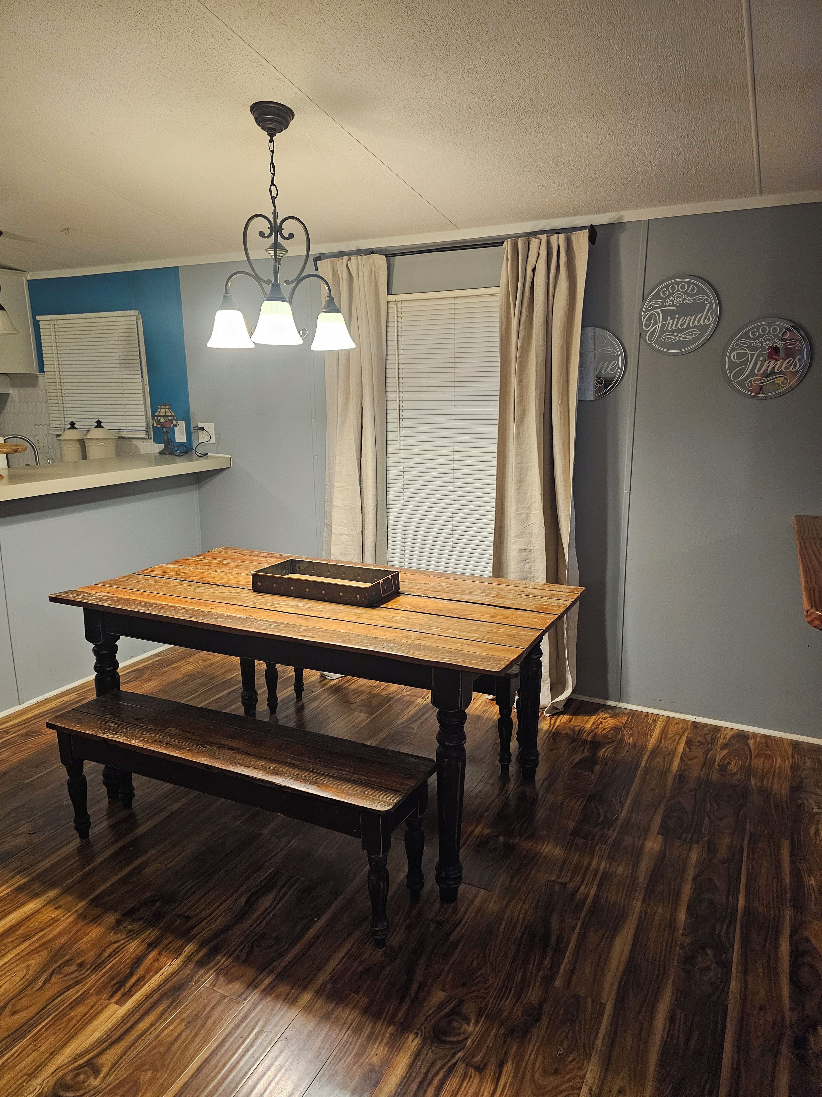 Un comedor con una mesa y banco de madera, una lámpara colgante, una ventana con cortinas y decoraciones en la pared.