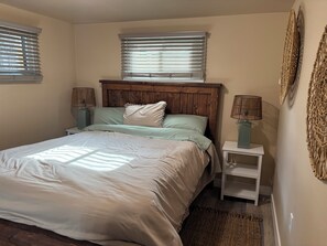 Ein Schlafzimmer mit einem Bett, zwei Nachttischen mit Lampen, einem Holz-Kopfteil und zwei Fenstern mit Jalousien.