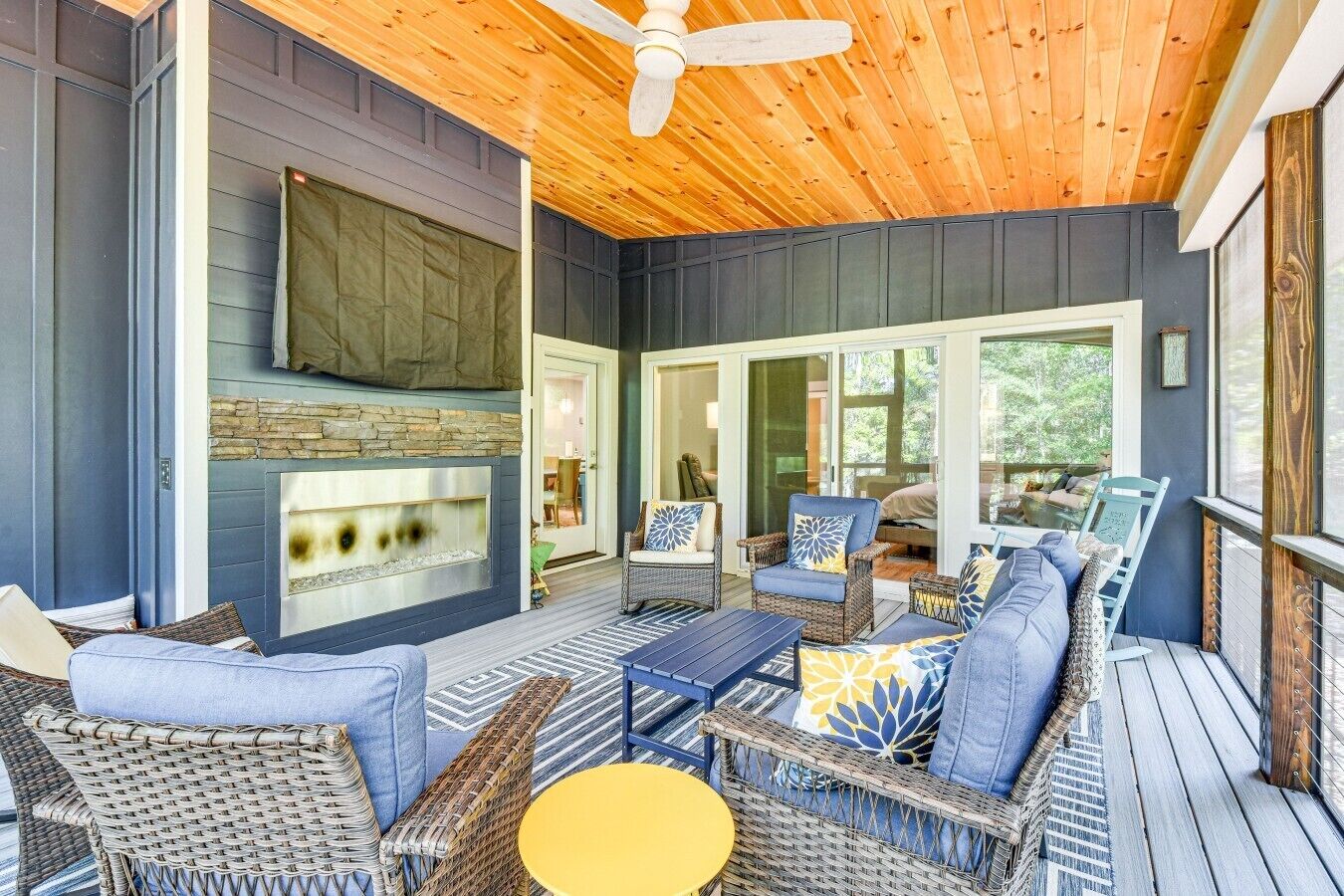 A covered outdoor seating area with wicker furniture, a stone fireplace, and a ceiling fan.
