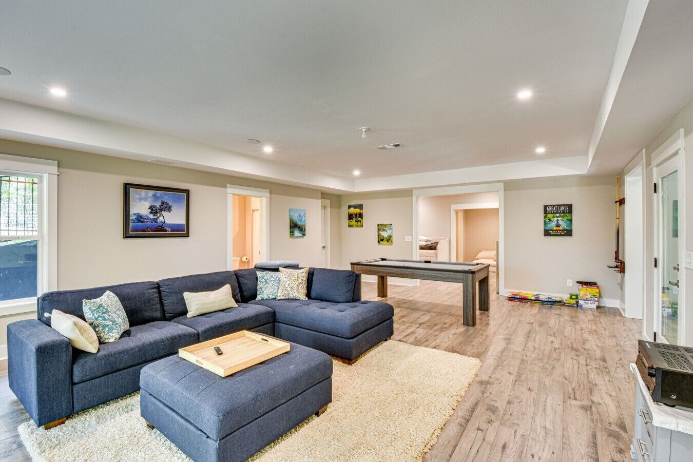 A modern living room with a sectional sofa, a pool table, and a billiards set.
