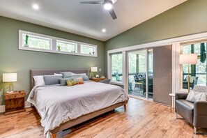 A bedroom with a large bed, a nightstand, a lamp, and a view of the outdoors through a sliding glass door. - Waterfront Home on Lake Hartwell w/ Dock Access (Hartwell)