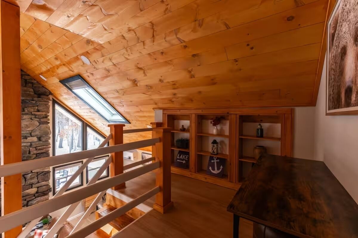 Ein Holzinnenraum mit schrägverdeckter Decke, einer Steinwand und einer Holztreppe.