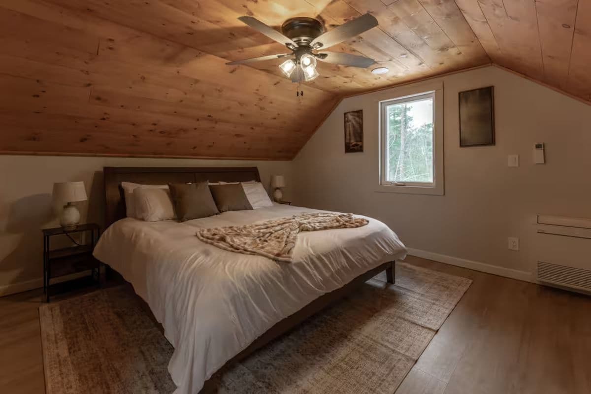 Ein Schlafzimmer mit einem Bett, einem Nachttisch, einem Deckenventilator, einem Fenster und einem Wandheizgerät.