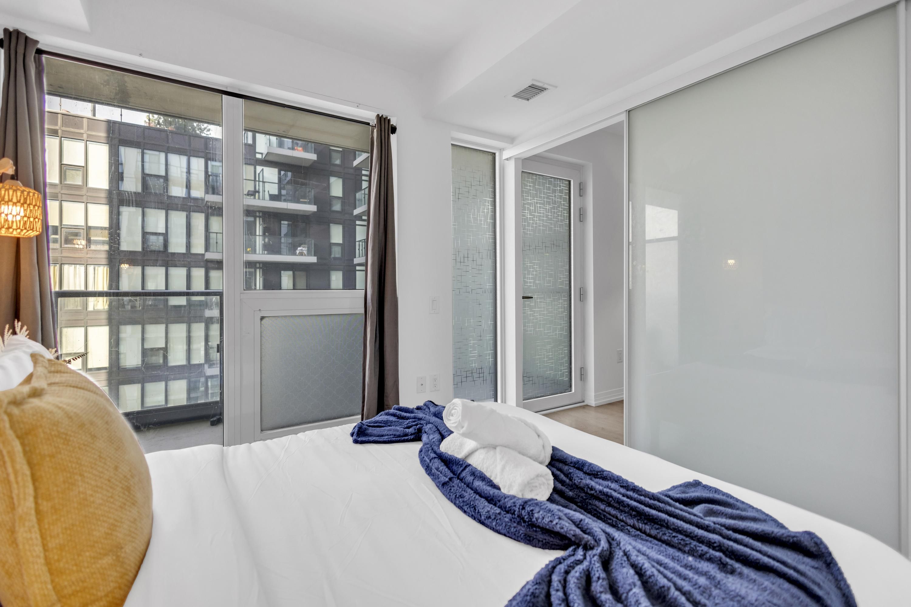 Hotelkamer met een groot bed, uitzicht op een gebouw door het raam en een schuifpui naar een balkon.