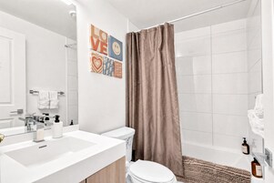 Um banheiro moderno com pia, vaso sanitário e cortina de chuveiro brancos.