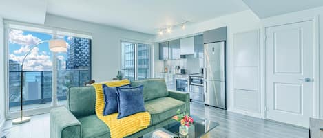 A modern apartment with a green sofa, a glass coffee table, and a view of the city through large windows.