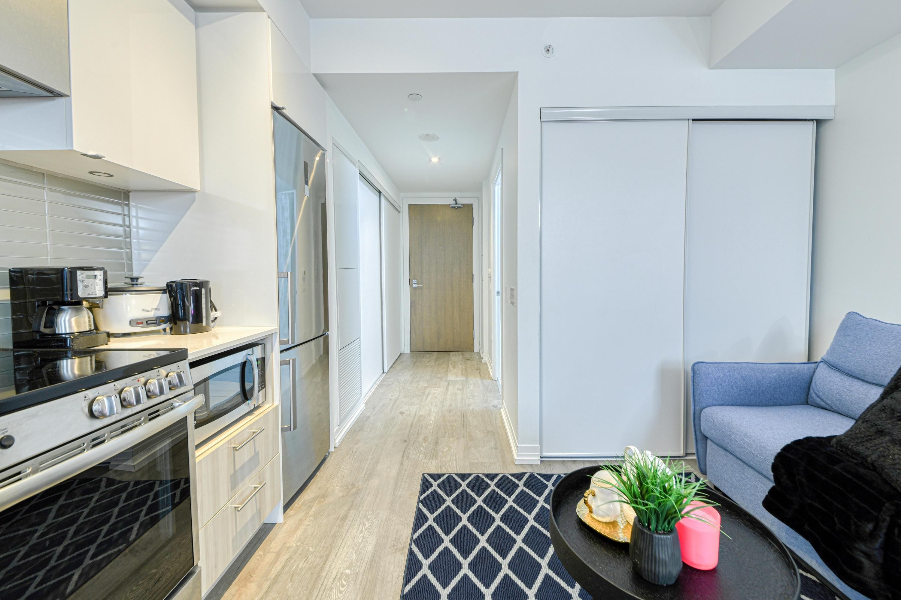 A modern kitchen with a stove, microwave, and coffee maker, a dining area with a table and chairs, and a living room with a sofa.