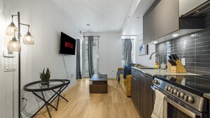 A modern kitchen with a built-in oven, a dining area with a round table and chairs, and a flat-screen TV mounted on the wall.
