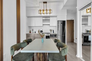 Una cocina moderna con armarios blancos, una isla central y un comedor con sillas tapizadas en verde.