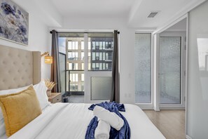 Quarto de hotel com uma cama grande, mesa de cabeceira, abajur e vista para o exterior.