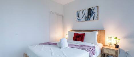 A bedroom with a bed, bedside table, lamp, and a painting on the wall.