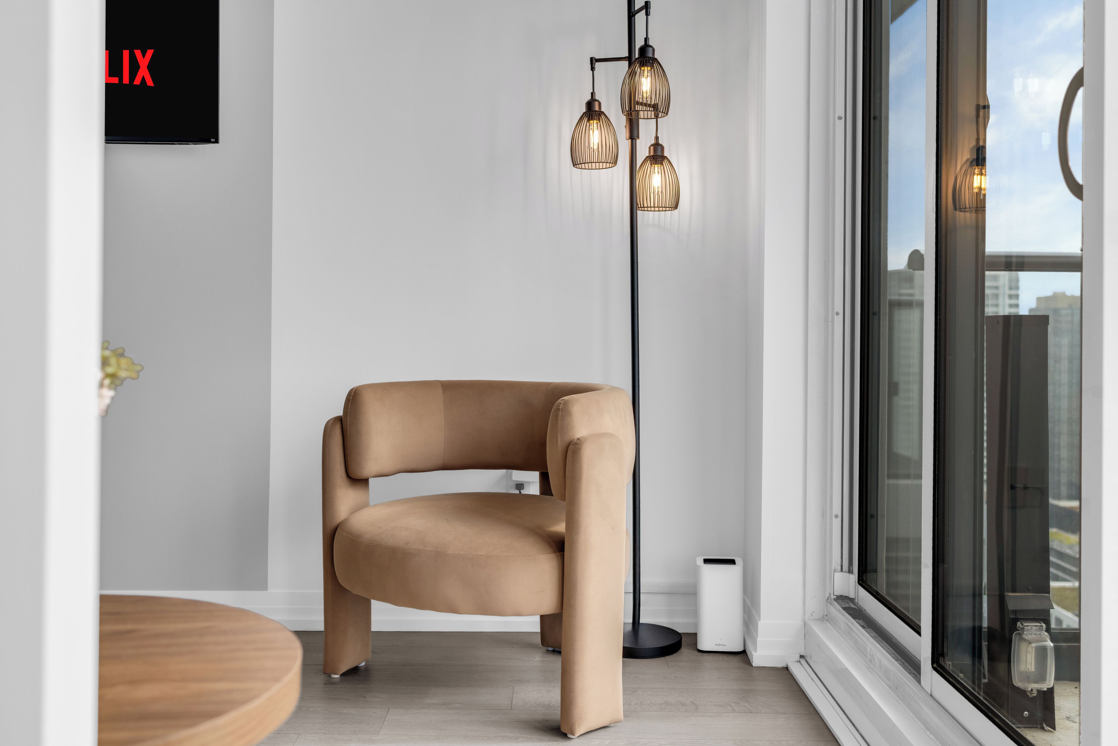Ein modernes Interieur mit einem braunen Ledersessel, einem runden Holztisch und einer Stehlampe mit drei Leuchten.