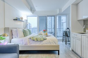 A modern bedroom with a large bed, a desk, and a view of the city through a sliding glass door.