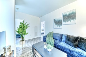 A modern living room with a blue sofa, a coffee table, a large green plant, and artwork on the wall.