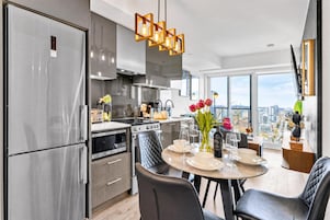 Een moderne keuken met roestvrijstalen apparatuur, een eethoek met een ronde tafel en stadszicht door grote ramen.