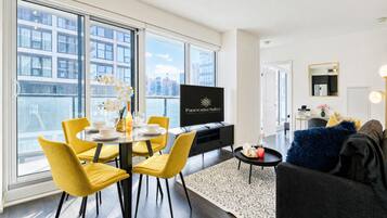 A modern living room with a dining area, a flat-screen TV, and a city view.