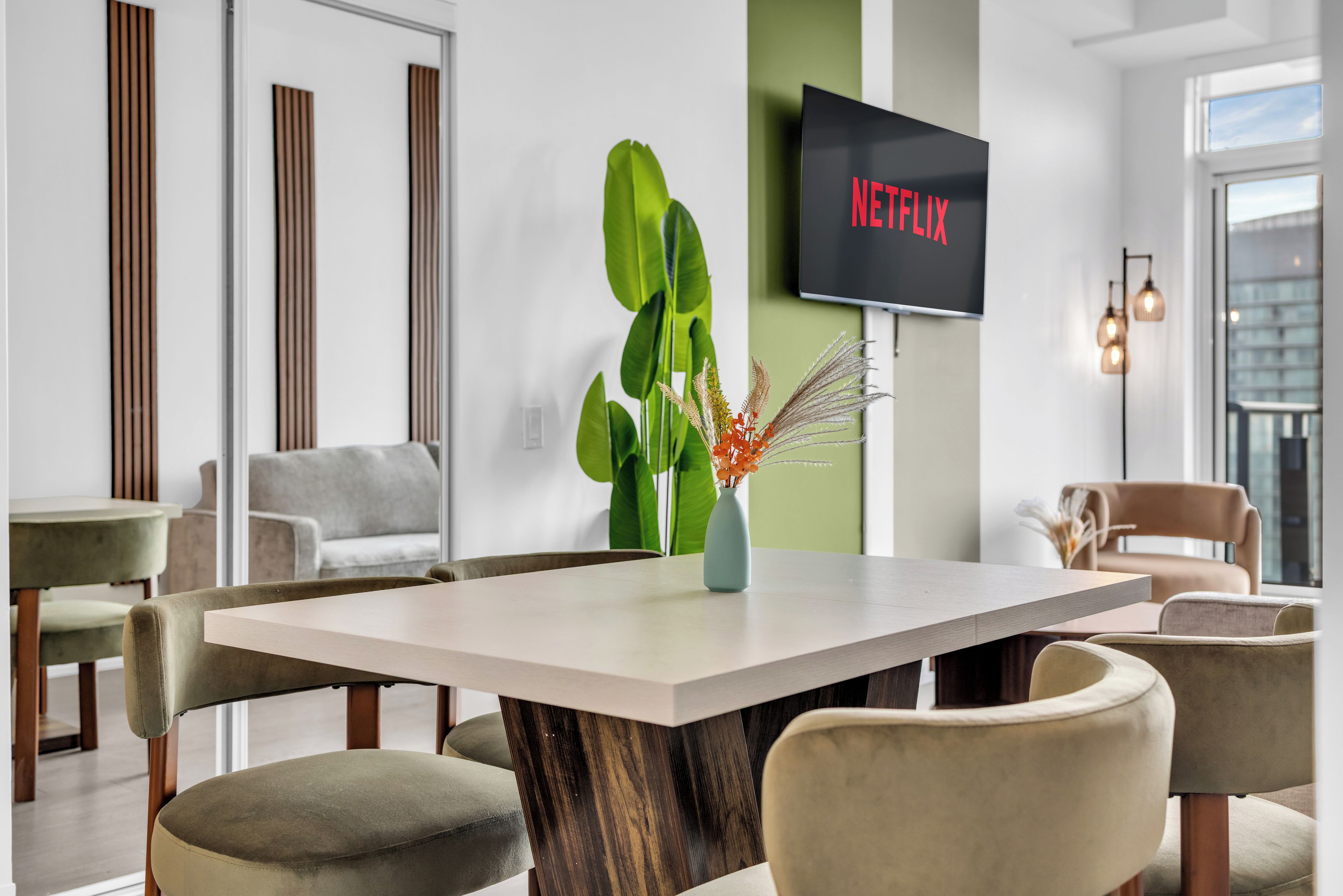 Ein modernes Interieur mit einem großen Tisch, Stühlen, einer Pflanze und einem Fernseher, der 'NETFLIX' anzeigt.