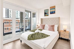A hotel room with a large bed, a view of the city through a sliding door, and two framed pictures on the wall.