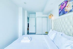 Hotelkamer met een groot bed, een gestapeld hoofdeinde, een schilderij aan de muur en een deur naar een badkamer.