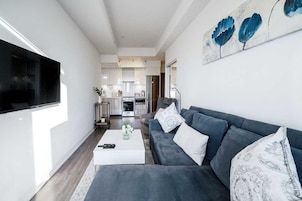 Een moderne woonkamer met een grijze bank, een witte salontafel en een flatscreen televisie aan de muur.
